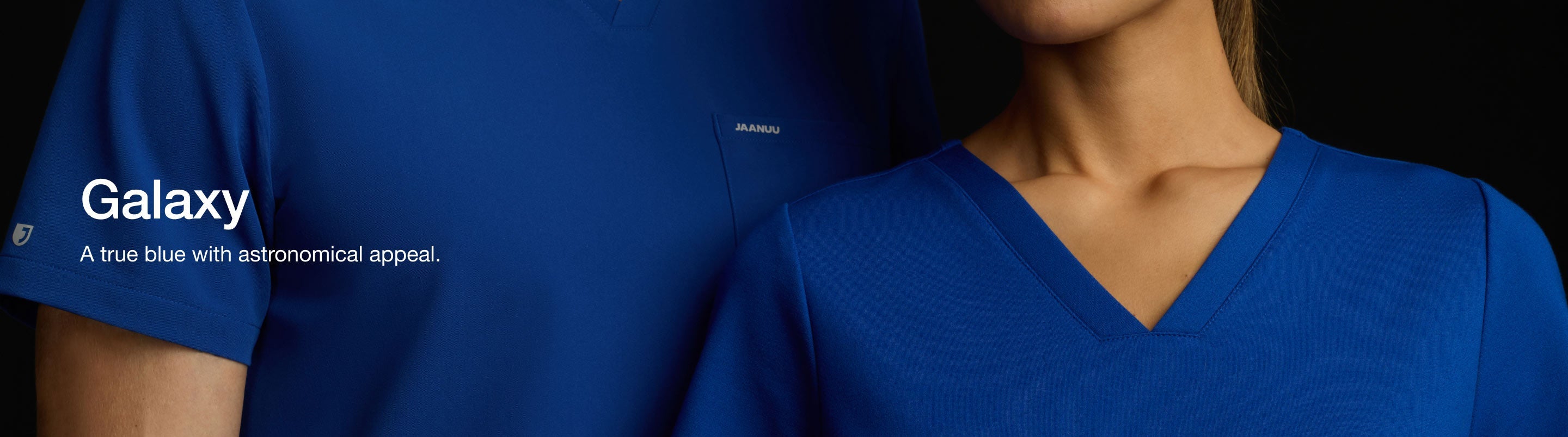 Image of a man and woman wearing JAANUU Galaxy color scrubs. Image is a close zoom around the chest level with their faces cropped out. Image has text, "Galaxy: A true blue with astronomical appeal."