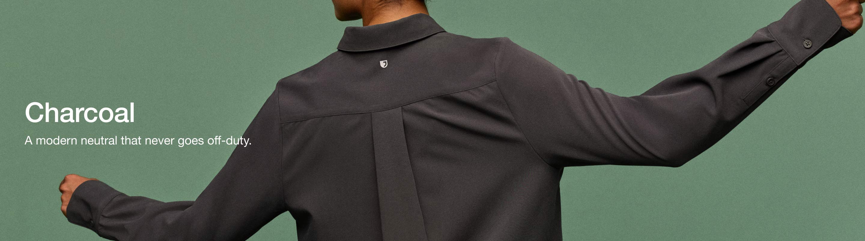 Image of woman wearing JAANUU Charcoal colored scrubs. Image has text saying, "Charcoal: A modern neutral that never goes off-duty."