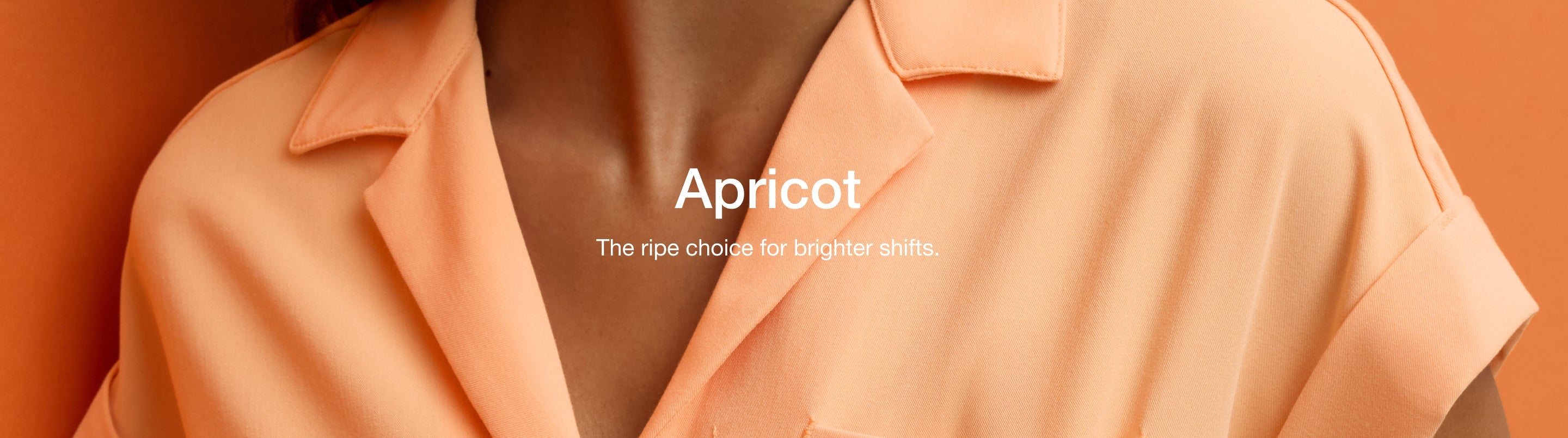 Close-up of a woman wearing a Jaanuu Apricot (peachy orange) collared scrub top on an orange background, with text 'Apricot' and 'The ripe choice for brighter shifts.'