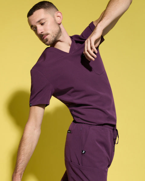 Image of a man wearing JAANUU scrubs in Deep Eggplant color. - Men Nav Tile