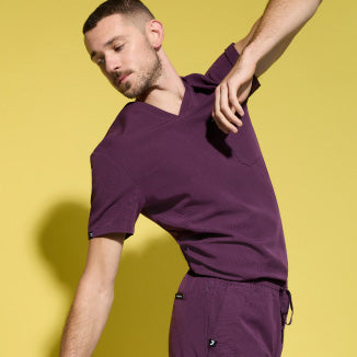 Image of a man wearing JAANUU scrubs in Deep Eggplant color. - Men Nav Tile