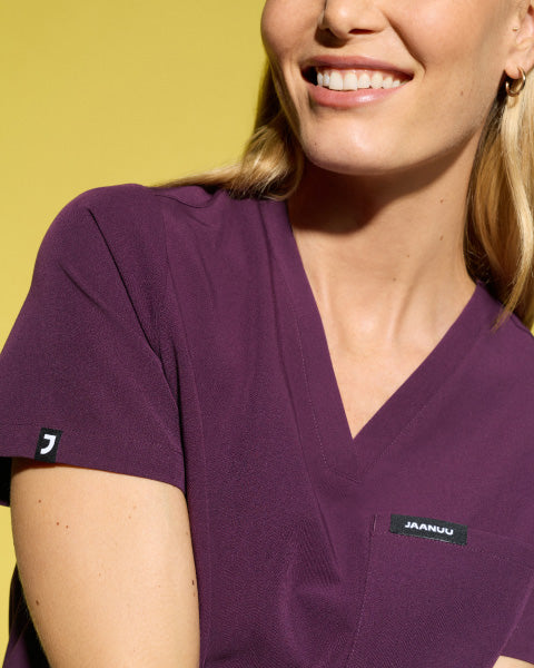 Image of a woman wearing JAANUU scrubs in Deep Eggplant color. - Women Nav Tile