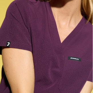 Image of a woman wearing JAANUU scrubs in Deep Eggplant color. - Women Nav Tile