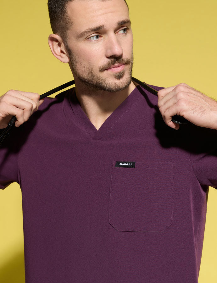 A man wearing JAANUU scrubs in Deep Eggplant color while holding a stethoscope around his neck.
