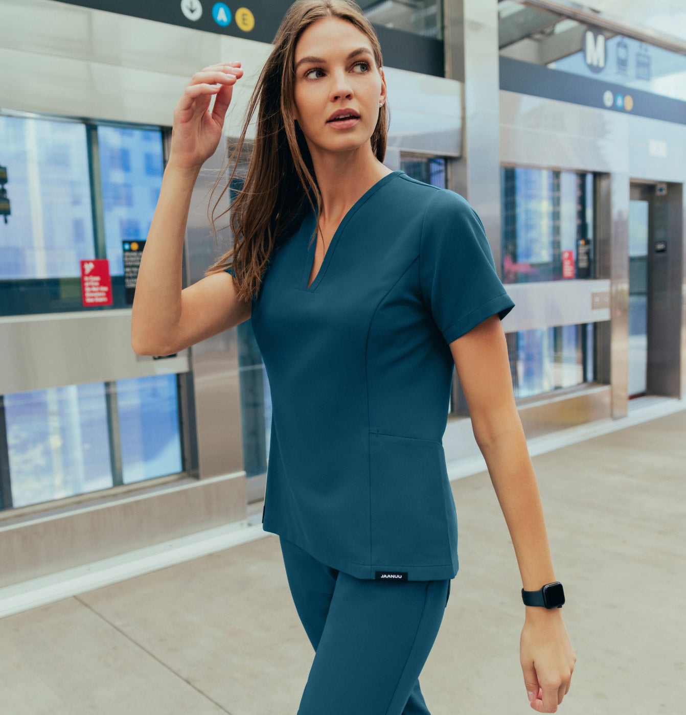 A woman wearing JAANUU scrubs walking on a sidewalk.