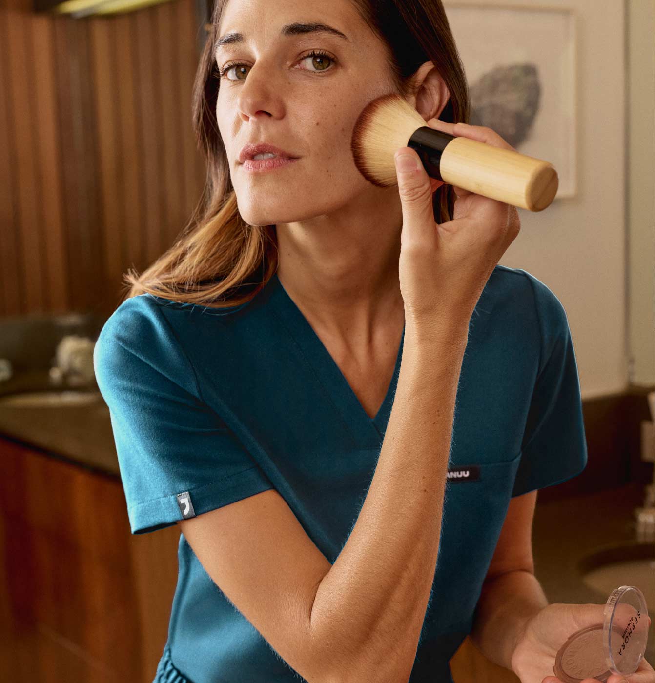 A woman wearing scrubs doing her makeup.