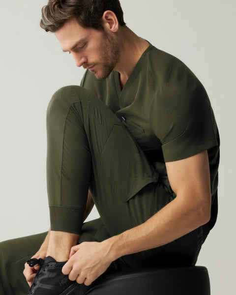 A man wearing JAANUU Deep Olive colored scrubs. - Men Nav Tile
