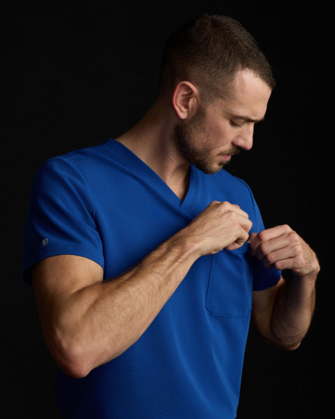 A man wearing JAANUU scrubs in Galaxy color while adjusting his chest pocket. - Men Nav Tile