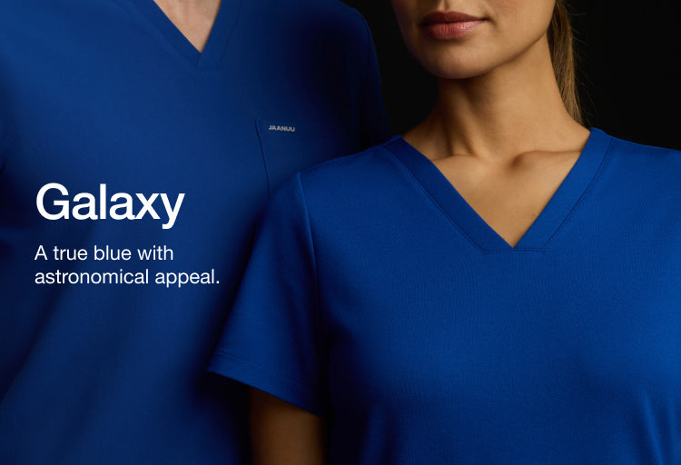 Image of a man and woman wearing JAANUU Galaxy color scrubs. Image is a close zoom around the chest level with their faces cropped out. Image has text, "Galaxy: A true blue with astronomical appeal."
