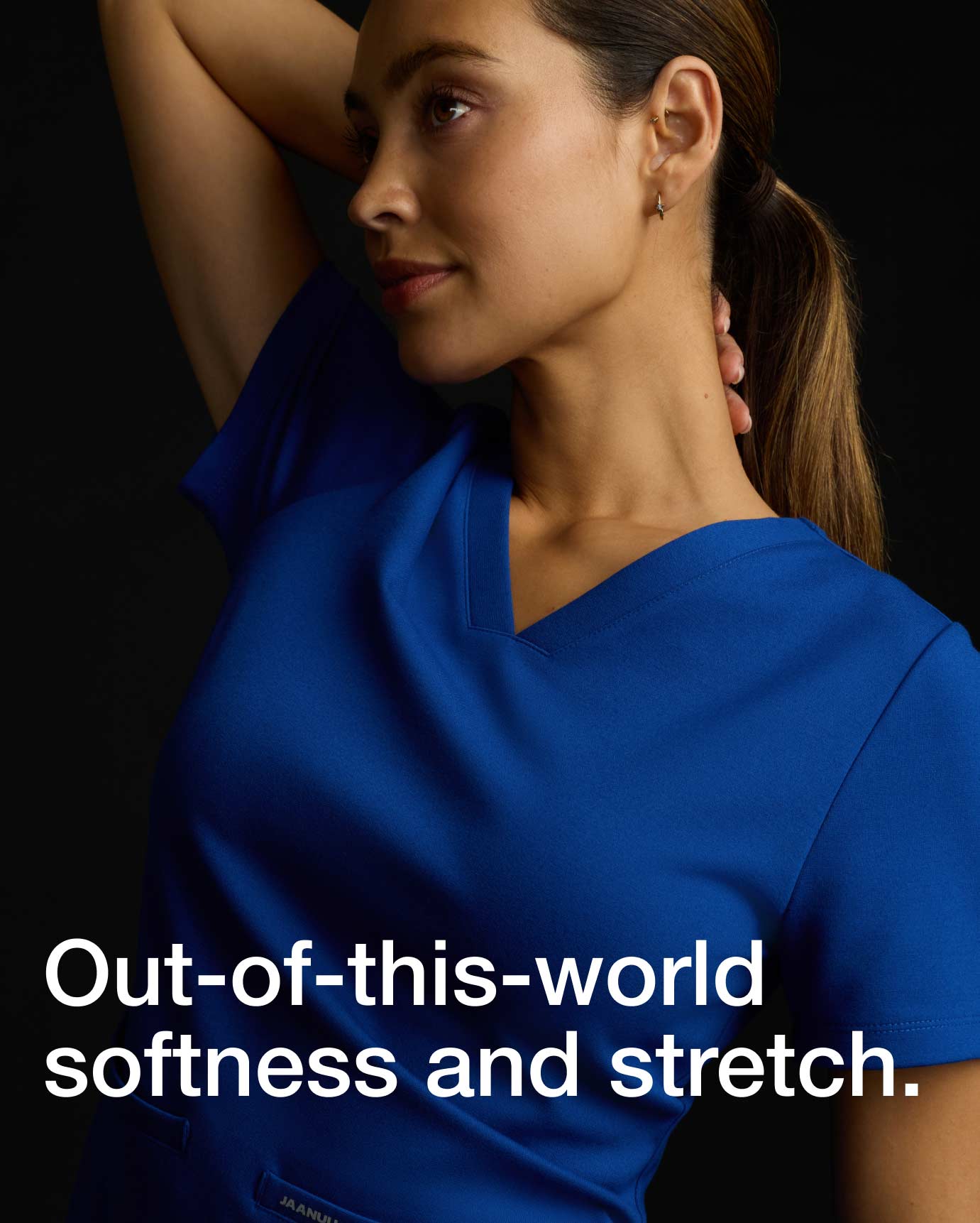 Image of a woman wearing JAANUU Galaxy color scrubs. "Image has text, "Out-of-this-world softness and stretch."