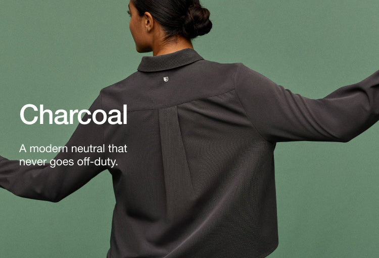 Image of woman wearing JAANUU Charcoal colored scrubs. Image has text saying, "Charcoal: A modern neutral that never goes off-duty."