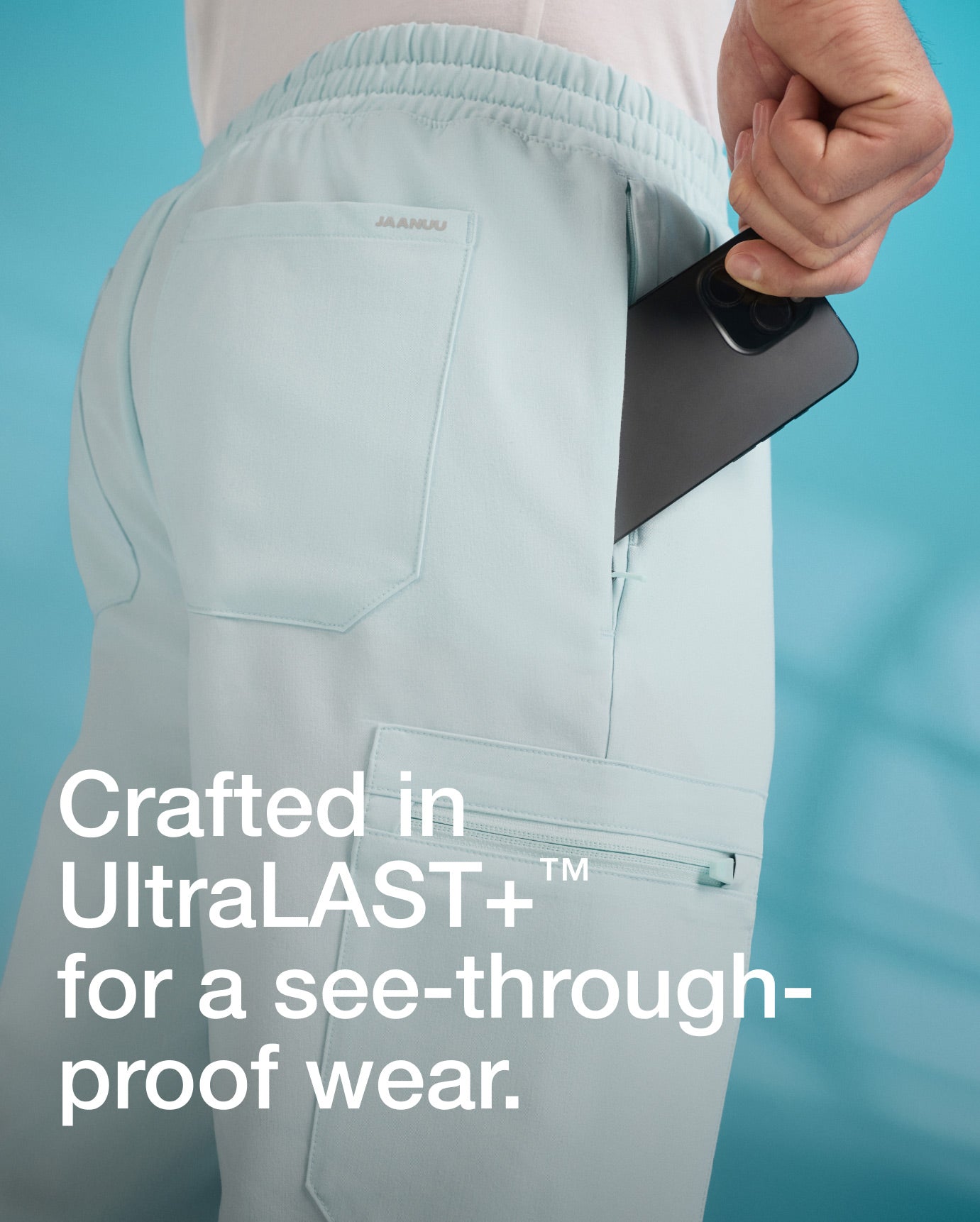 Image of a man wearing JAANUU Sky  Blue color scrub pant with a mobile device going into a side pocket. "Image has text, "Crafted in UltraLAST+ for a see-through-proof wear."