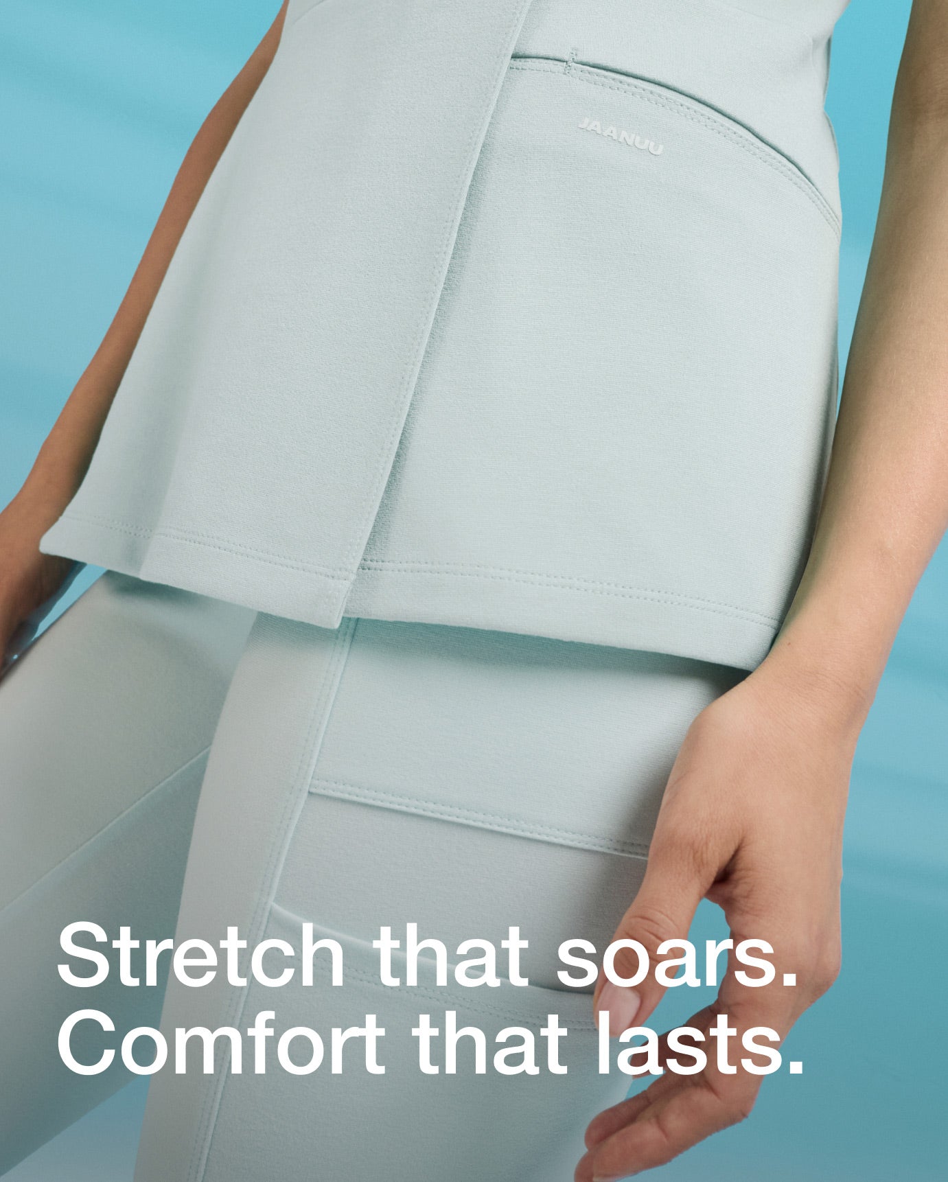 Image of a women wearing JAANUU Sky Blue color scrubs. "Image has text, "Stretch that soars. Comfort that lasts."