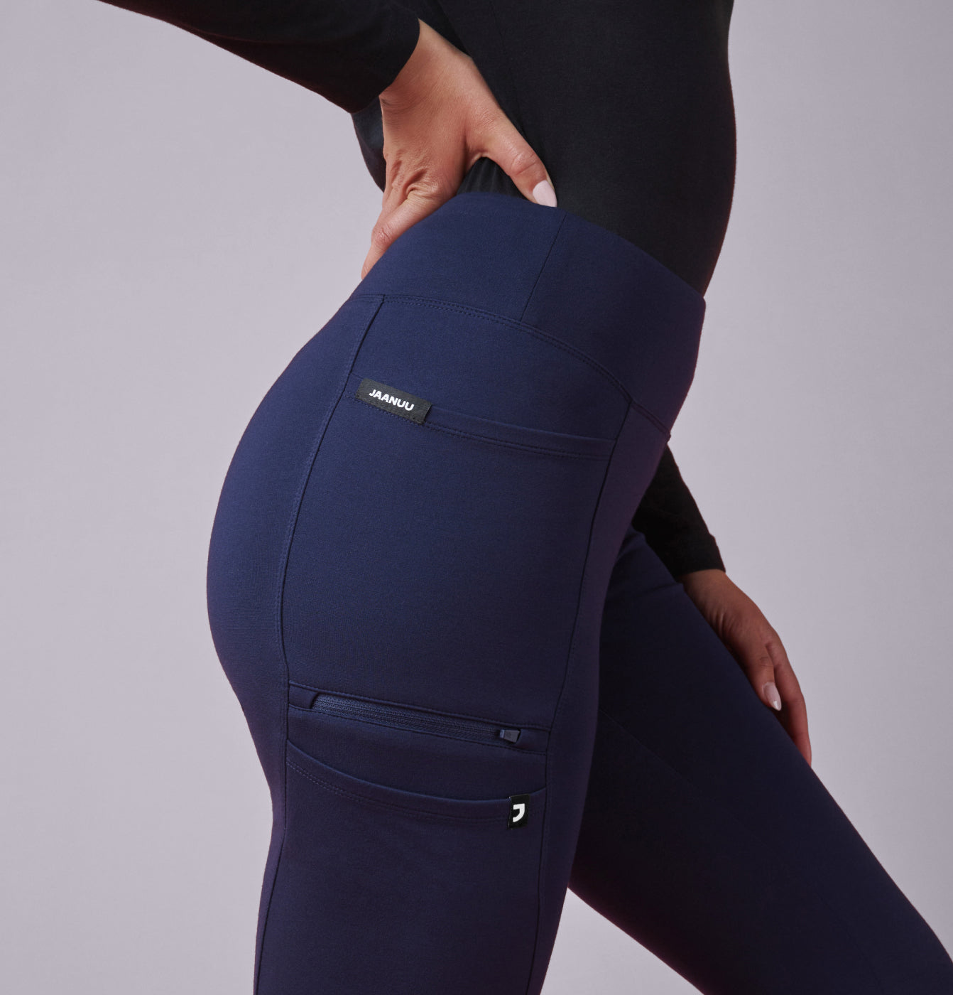 A women wearing Midnight Blue scrub pant and a Black underscrub with the JAANUU brand logo on a gray background