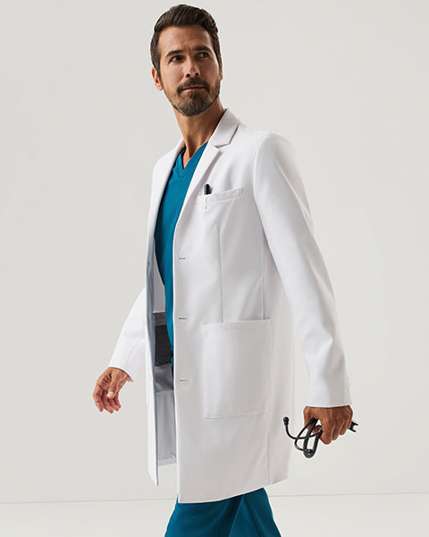 Man walking in white Jaanuu lab coat over teal scrubs, holding a stethoscope, on a light gray background - Men Nav Tile