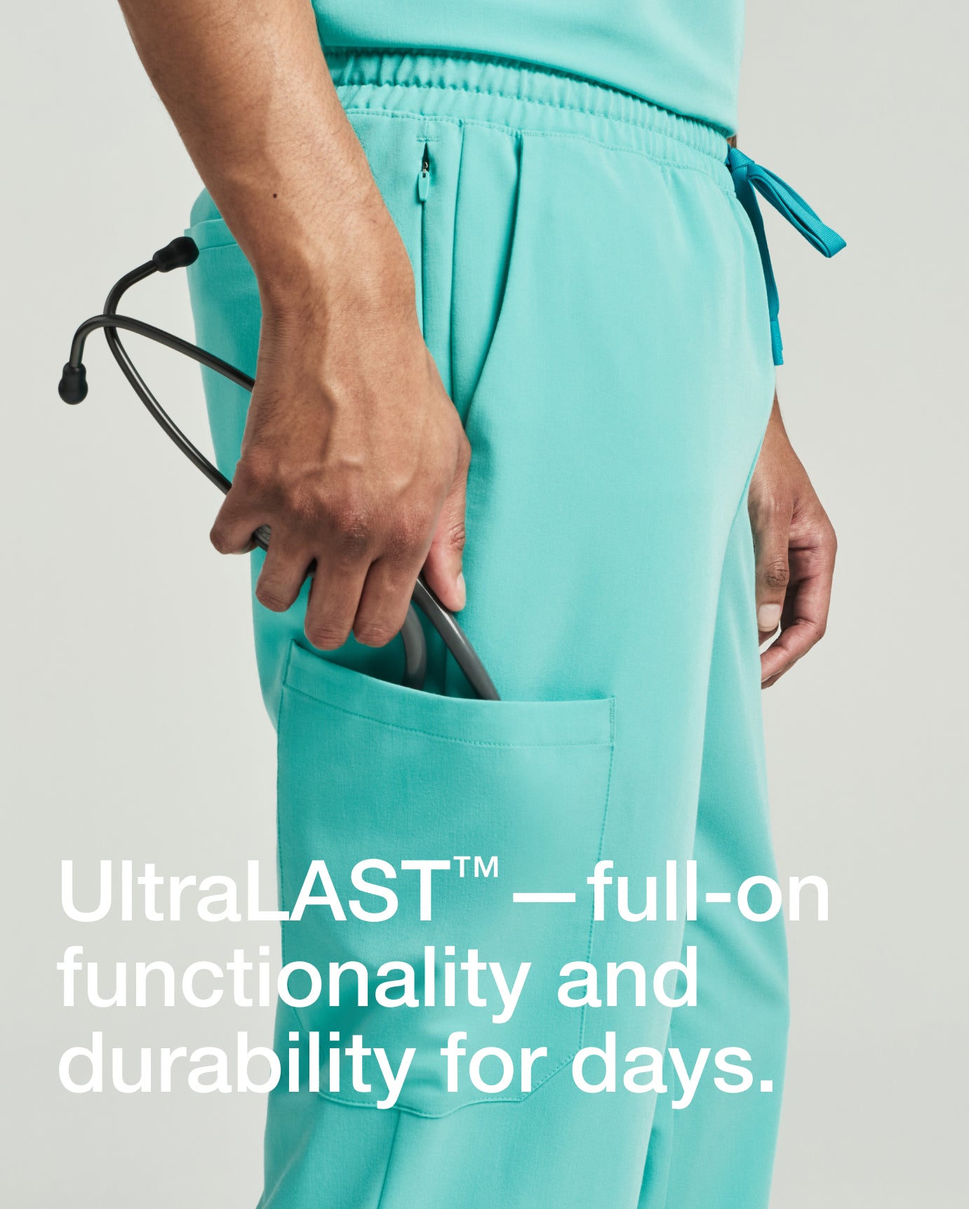 Close-up of a man wearing surf teal Jaanuu scrub joggers, reaching toward the cargo pocket where a stethoscope is tucked, with text 'UltraLAST™—full-on functionality and durability for days.'