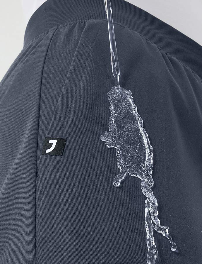 Image of water being poured on scrub pants with PFC-free water repellency. The water is rolling off the scrub pants.