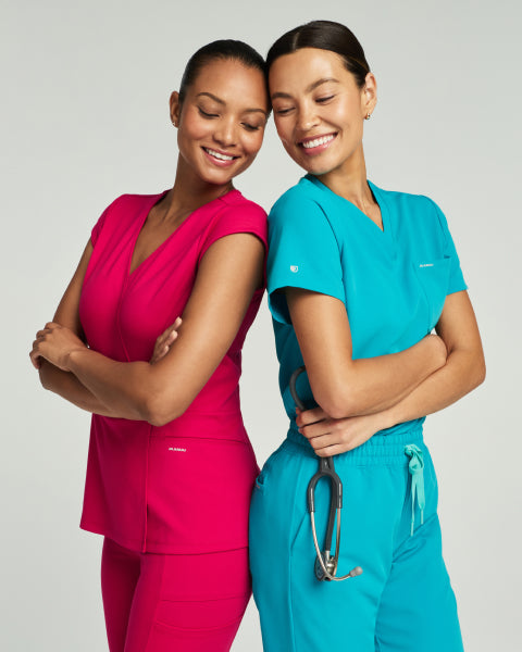 Two smiling women, one in a Sangria pink Jaanuu scrub set and one in a Marina teal scrub set. - Women Nav Tile