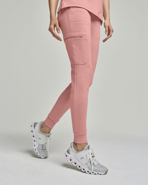 Woman wearing dusty rose Jaanuu scrub joggers with a side cargo pocket. - Women Nav Tile