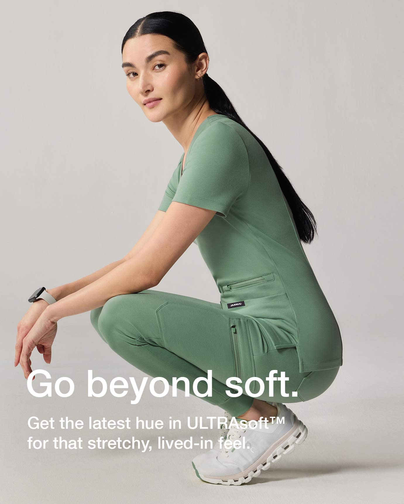 Women squatting in Sage scrubs with text, "Go beyond soft: Get the latest hue in LTRAsoft for that stretchy, lived-in feel.