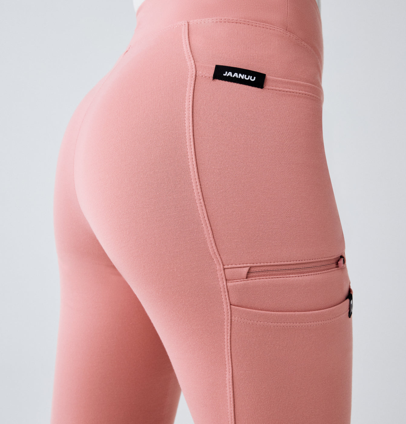 Close-up of pink UltraSOFT scrub pants with a zippered side pocket and JAANUU waistband label