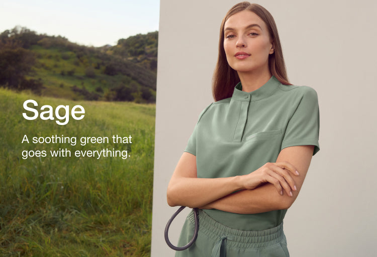 A woman in a sage green Jaanuu scrub top stands with her arms crossed before a white panel on a grassy hillside with mountains behind. Text on the image reads: "Sage. A soothing green that goes with everything."