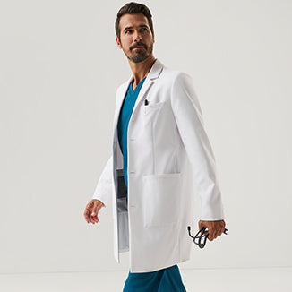 A man wearing a white Jaanuu lab coat over teal scrubs, holding a stethoscope - Men Nav Tile