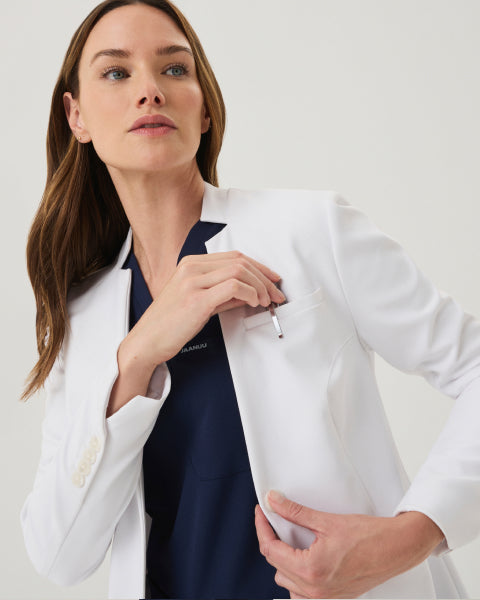 A woman wearing a white Jaanuu lab coat over a navy scrub top - Women Nav Tile