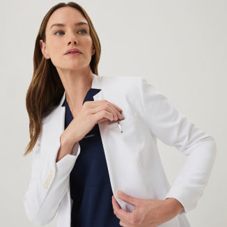 A woman wearing a white Jaanuu lab coat over a navy scrub top - Women Nav Tile