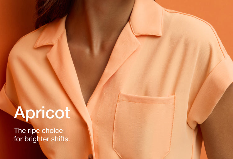 Close-up of a woman wearing a Jaanuu Apricot (peachy orange) collared scrub top on an orange background, with text 'Apricot' and 'The ripe choice for brighter shifts.'