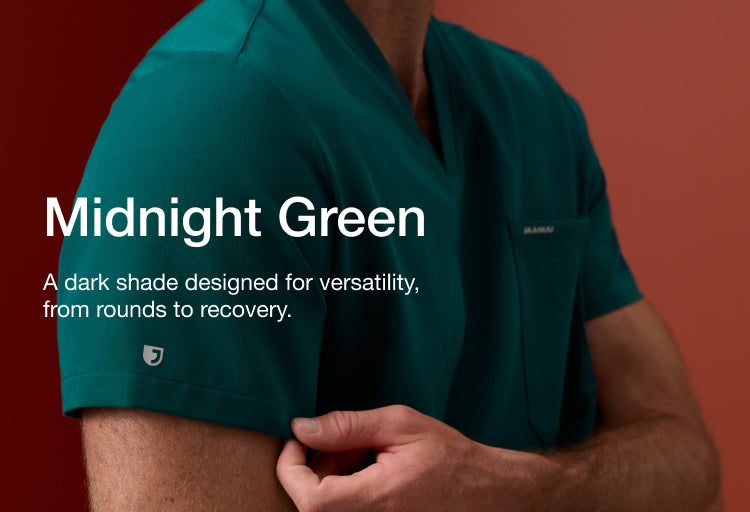 Man in a Midnight Green Jaanuu scrub top adjusting his sleeve, against a rust-red background. Text on the image reads: "Midnight Green. A dark shade designed for versatility, from rounds to recovery."