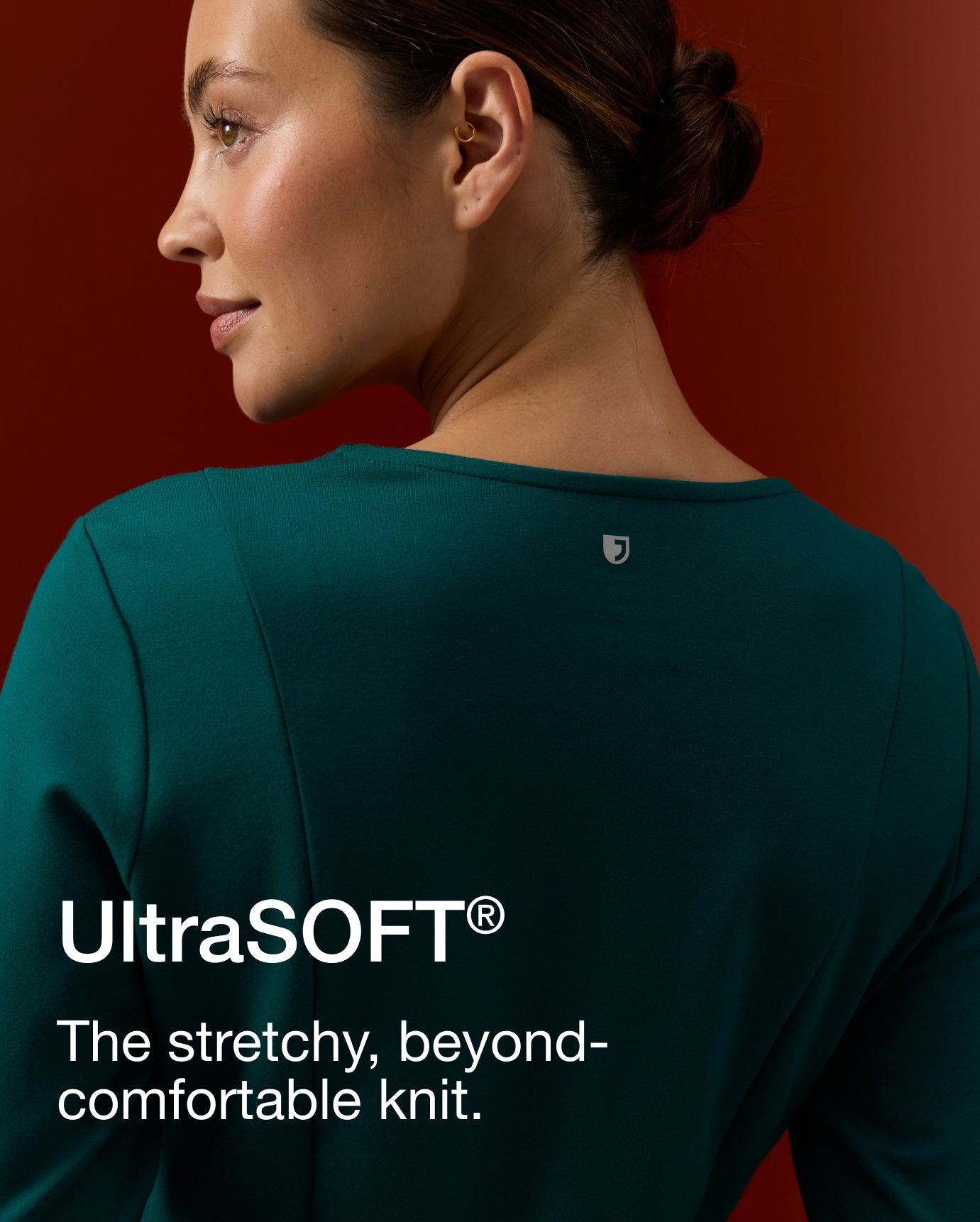 Rear profile of a woman wearing a Midnight Green UltraSOFT scrub top, hair in a low bun. Text on image reads: "UltraSOFT®. The stretchy, beyond-comfortable knit."