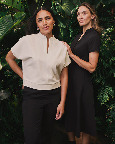 Two women standing. One is wearing fashionable scrubs and the other is wearing a scrub dress. - Women Nav Tile