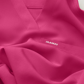 Close-up of a softly folded Jaanuu Warrior Pink (bright pink) V-neck scrub top with a chest pocket and a small white JAANUU logo printed on the pocket. - Women Nav Tile