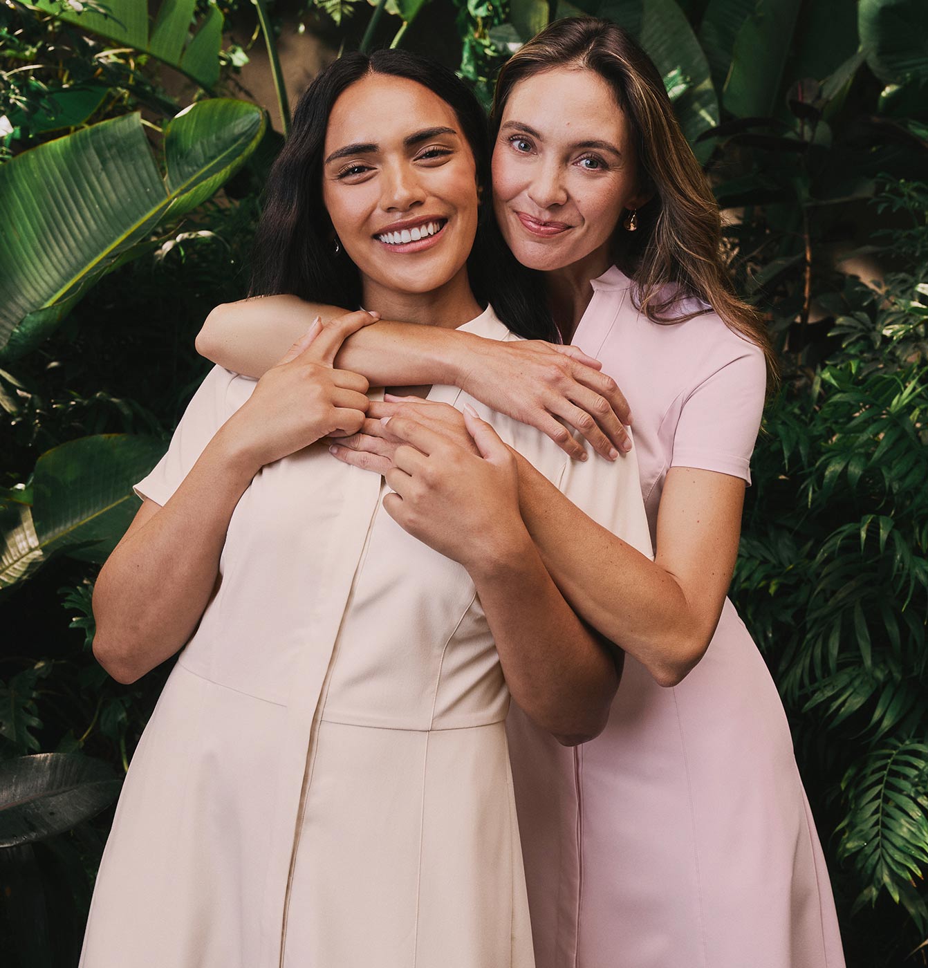 Two women in fashion capsule scrubs, background features tree and plant leaves.