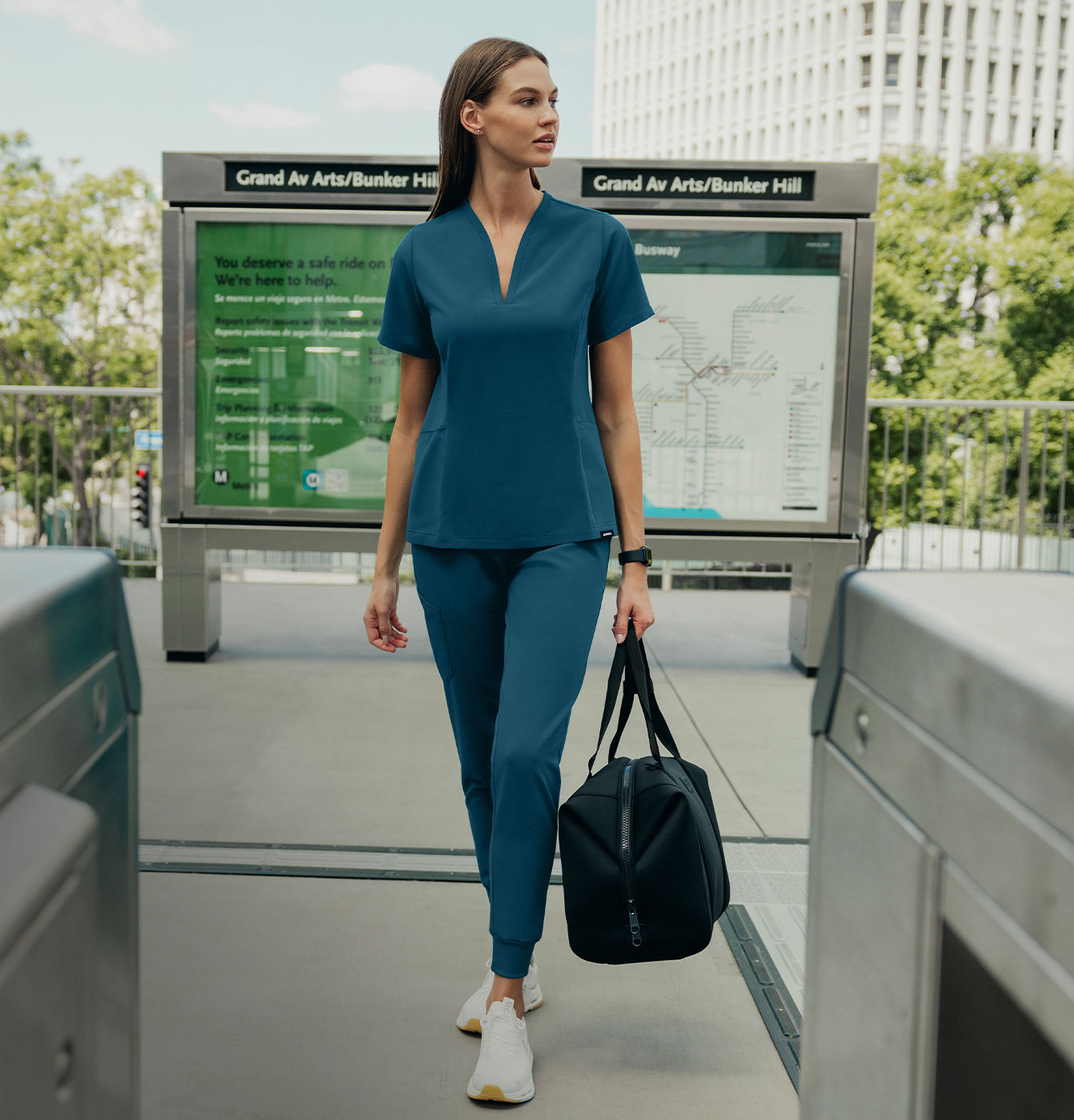 Woman wearing a scrub set walking near a subway station while carrying a bag.