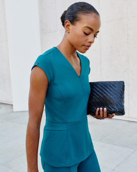 Woman wearing UltraSOFT scrubs holding a bag and walking outside. - Women Nav Tile