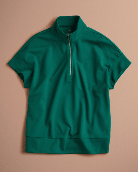 Animated flat lay that alternates between a Hunter Green (dark green) Jaanuu short-sleeve half-zip scrub top and matching flare-leg scrub pants with a zippered leg pocket, on a blush pink background. - Women Nav Tile
