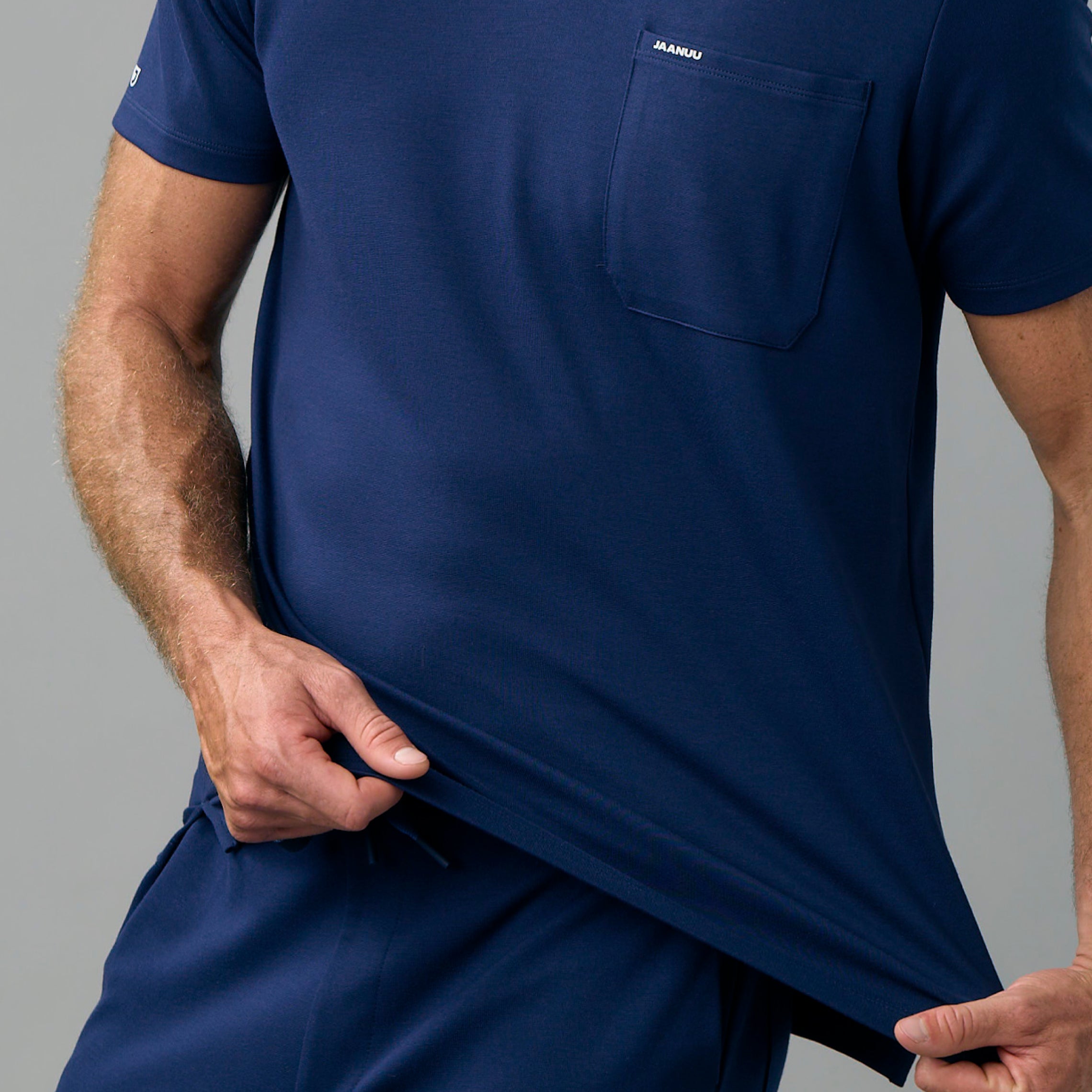 Man pulling down the hem of a navy UltraSOFT® scrub top with a chest pocket