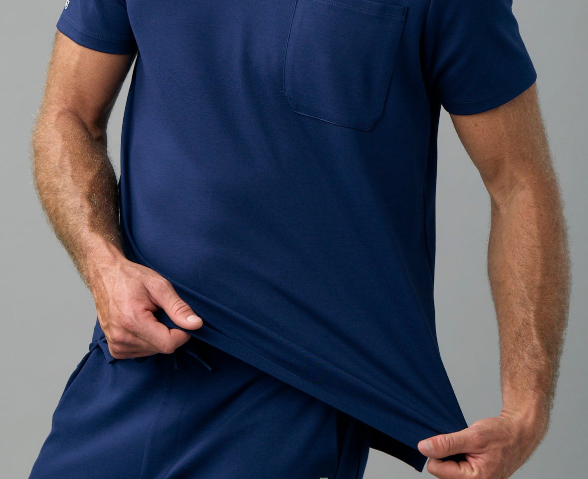 Man pulling down the hem of a navy UltraSOFT® scrub top with a chest pocket