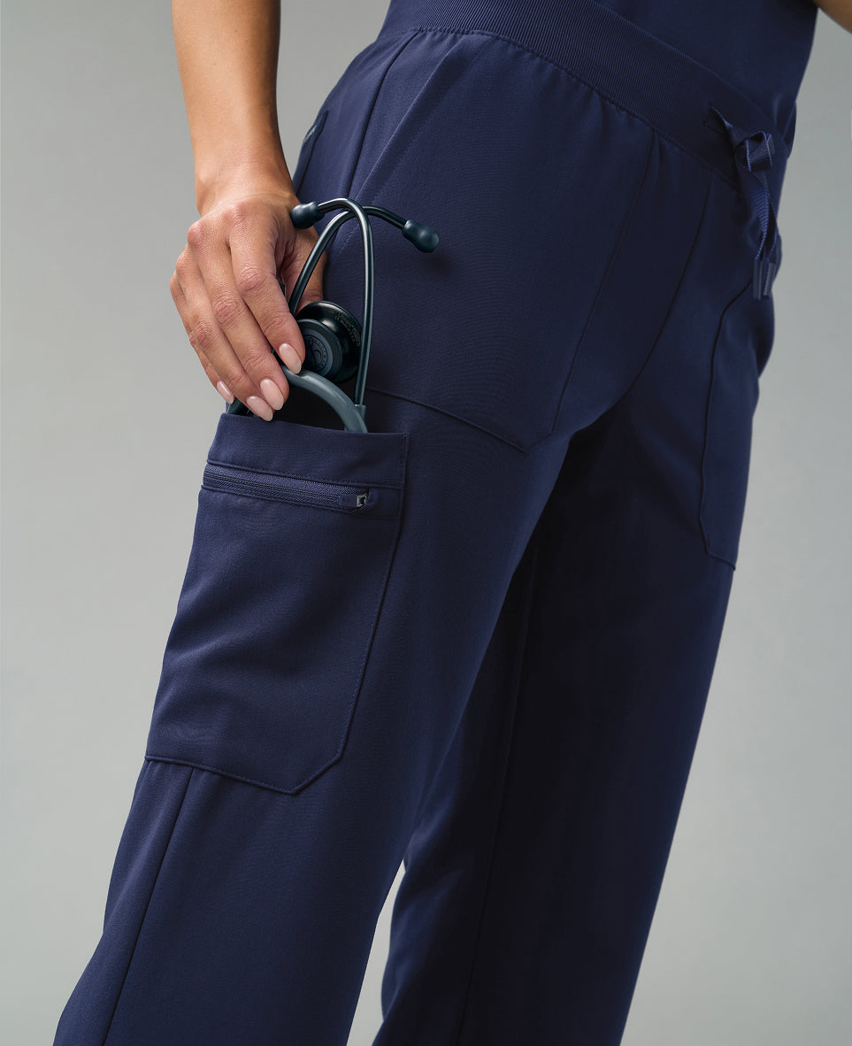 Detail of navy blue Jaanuu scrub pants as a hand slips a stethoscope into a cargo pocket
