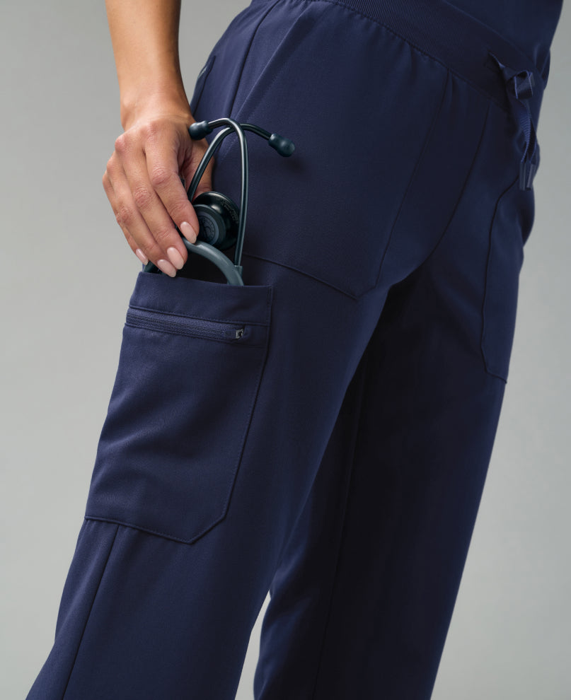 Detail of navy blue Jaanuu scrub pants as a hand slips a stethoscope into a cargo pocket