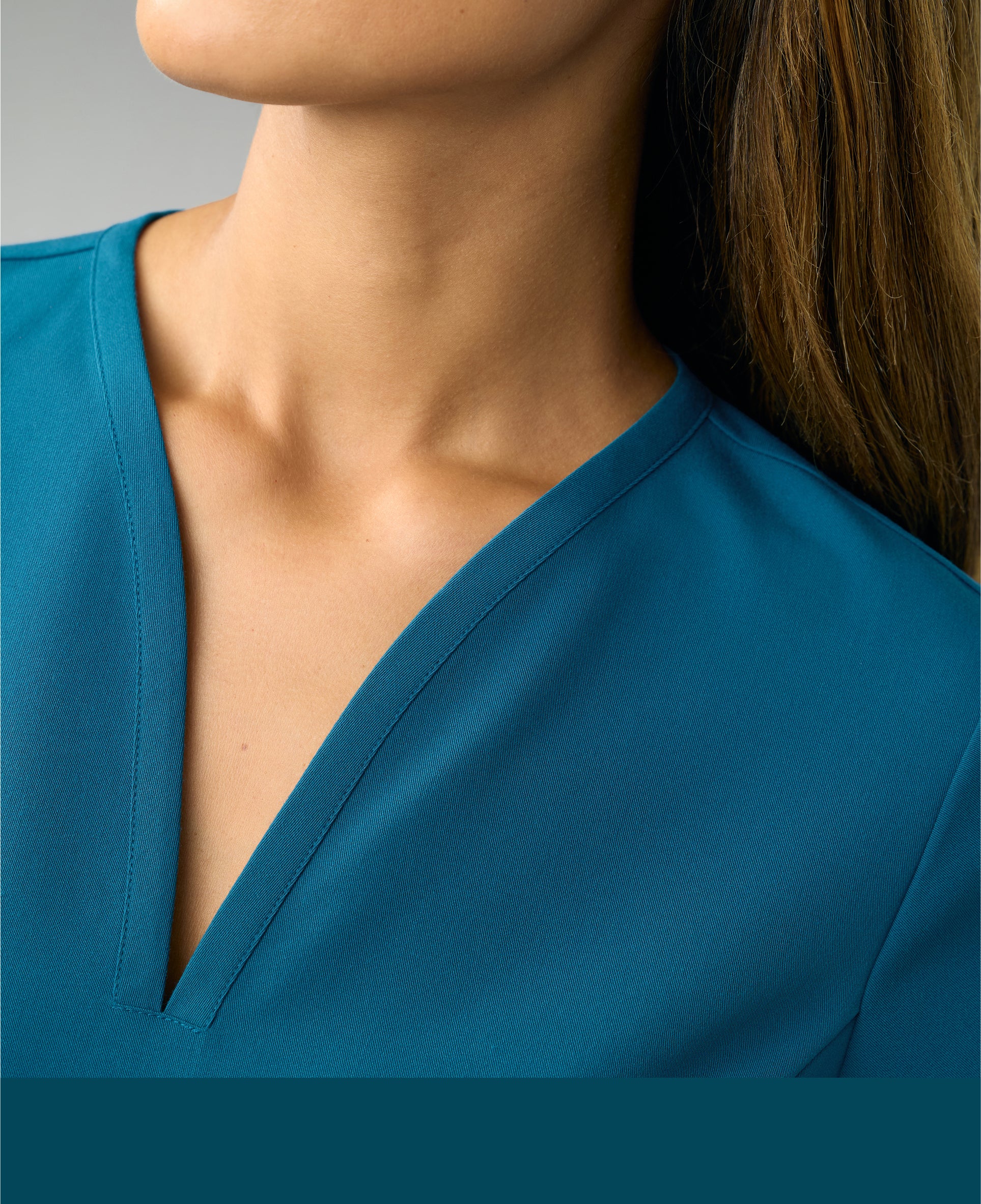 Close-up of the V-neckline of a caribbean blue Jaanuu scrub top, with a caribbean blue color band across the bottom