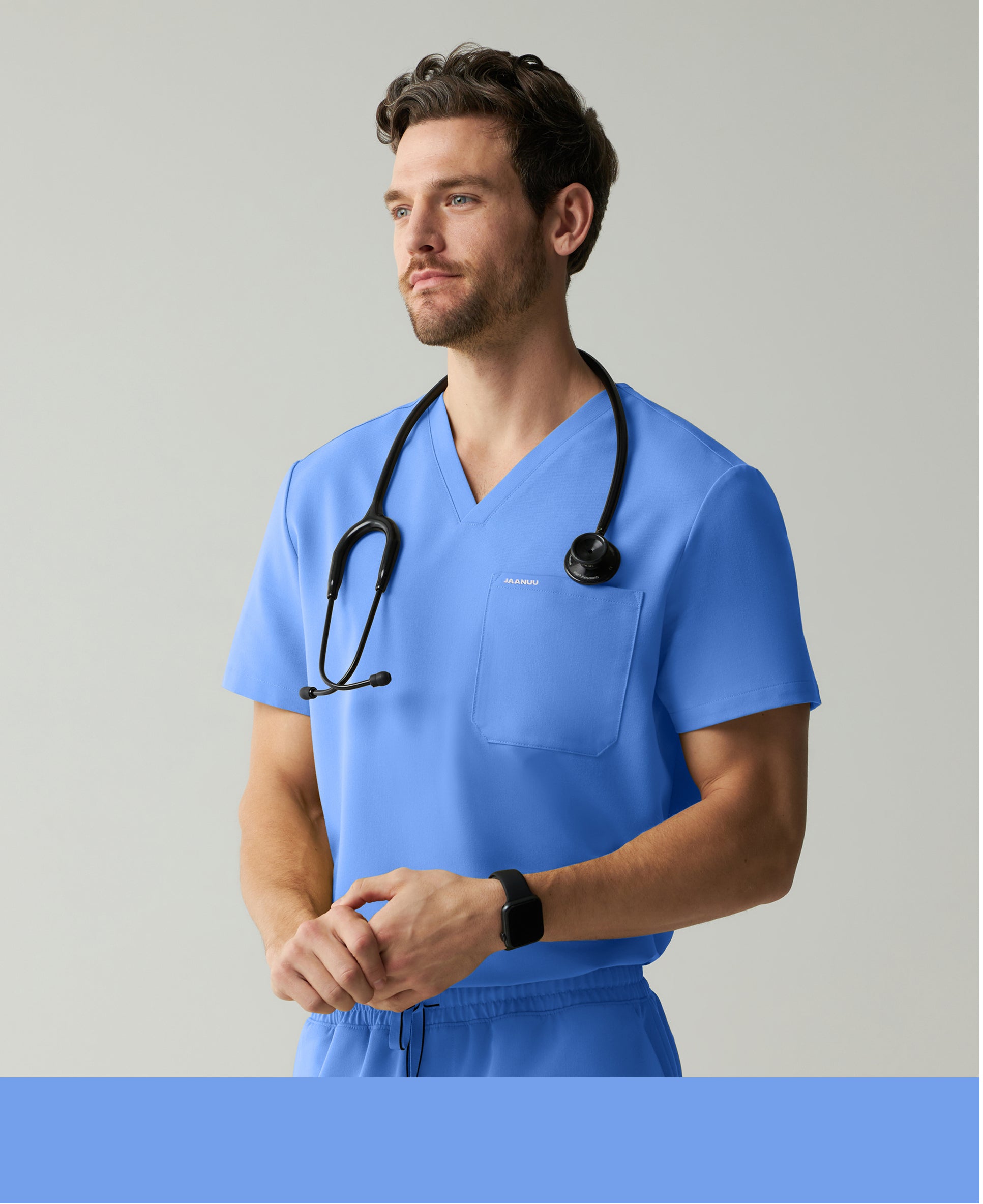 Man in a ceil blue Jaanuu V-neck scrub top and scrub pants with a stethoscope around his neck looking to the side against a light gray backdrop, with a ceil blue color band across the bottom