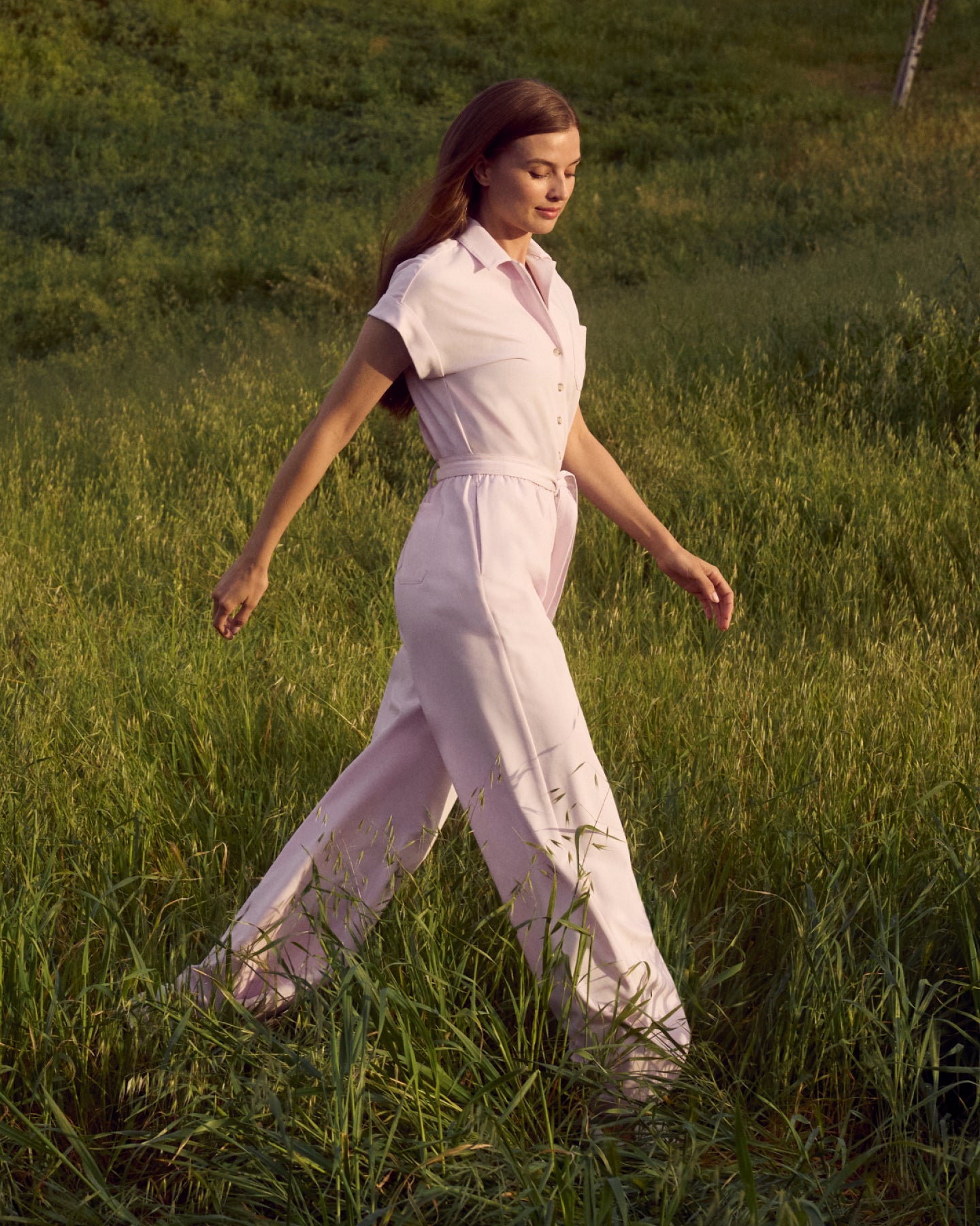 Woman walking through tall grass in a light pink short-sleeve jumpsuit