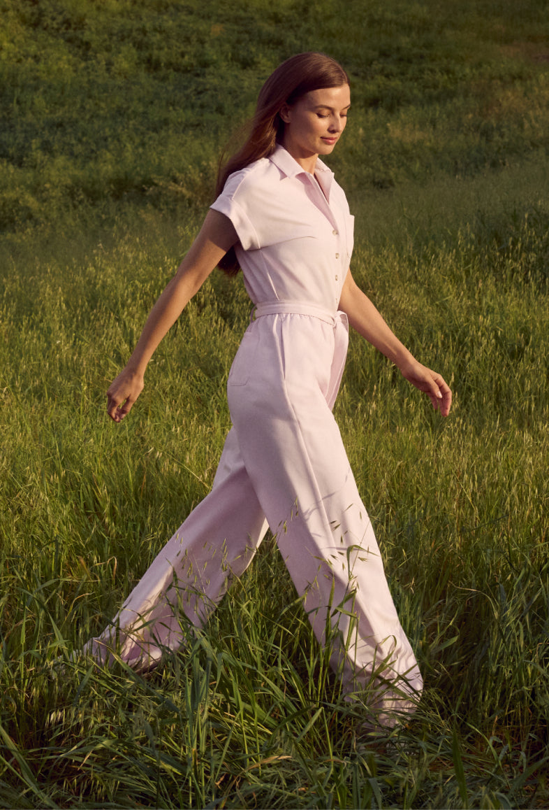 Woman walking through tall grass in a light pink short-sleeve jumpsuit