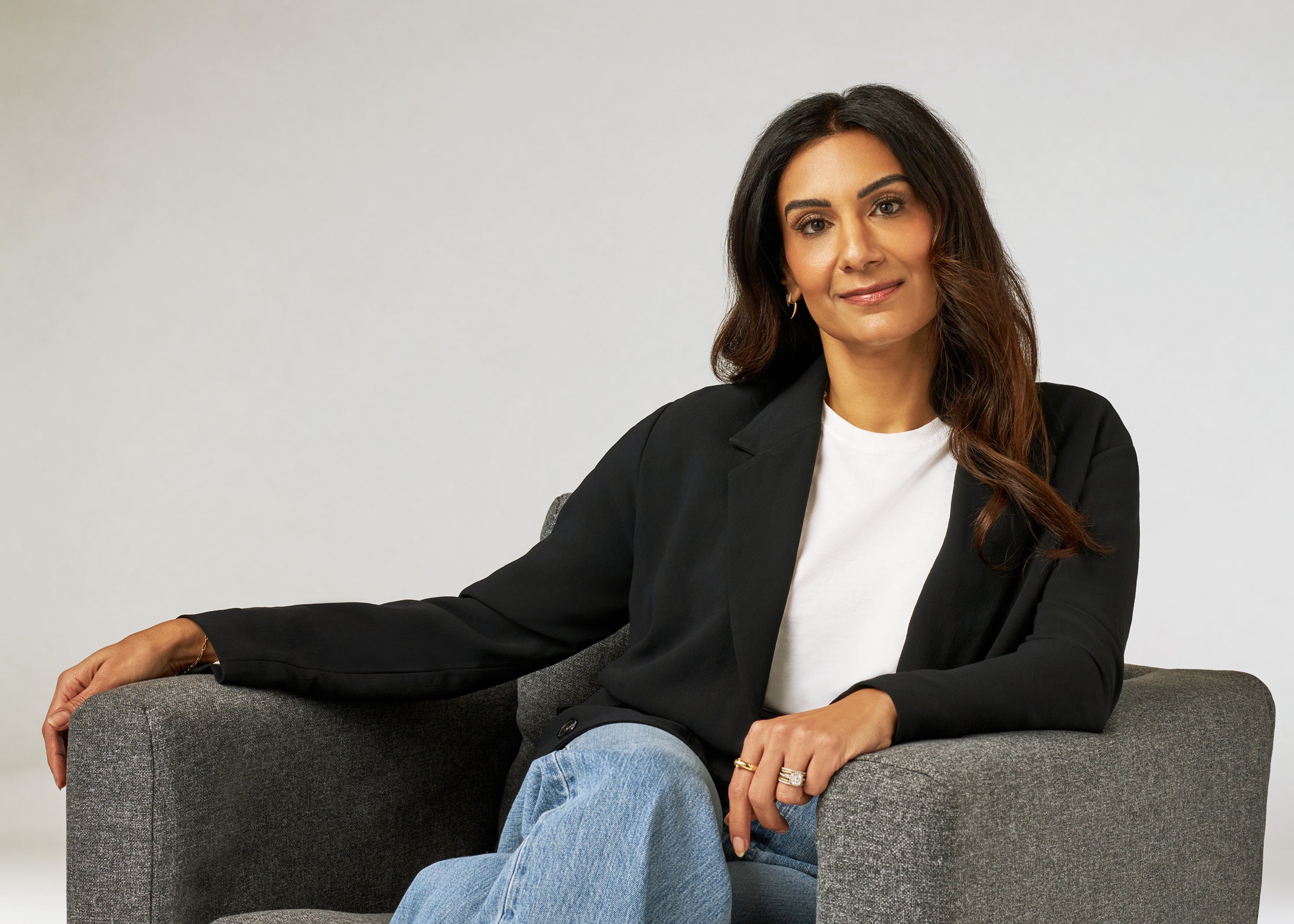 Dr. Neela, the practicing pediatrician behind JAANUU, seated in a gray armchair in a black blazer, white T-shirt and jeans