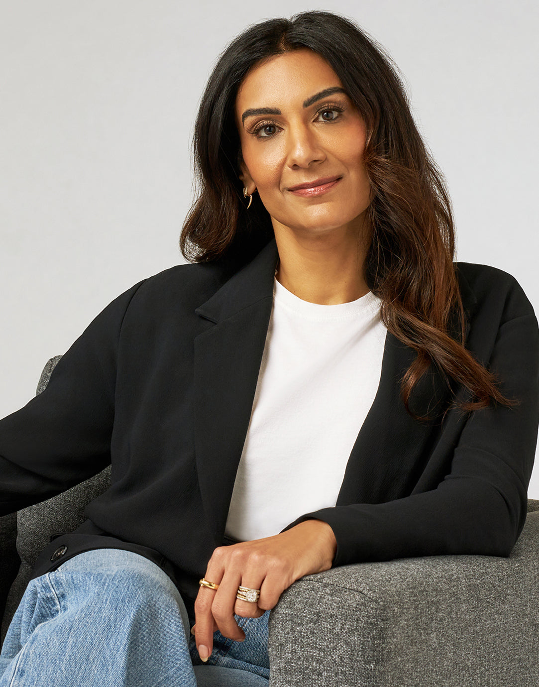 Dr. Neela, the practicing pediatrician behind JAANUU, seated in a gray armchair in a black blazer, white T-shirt and jeans