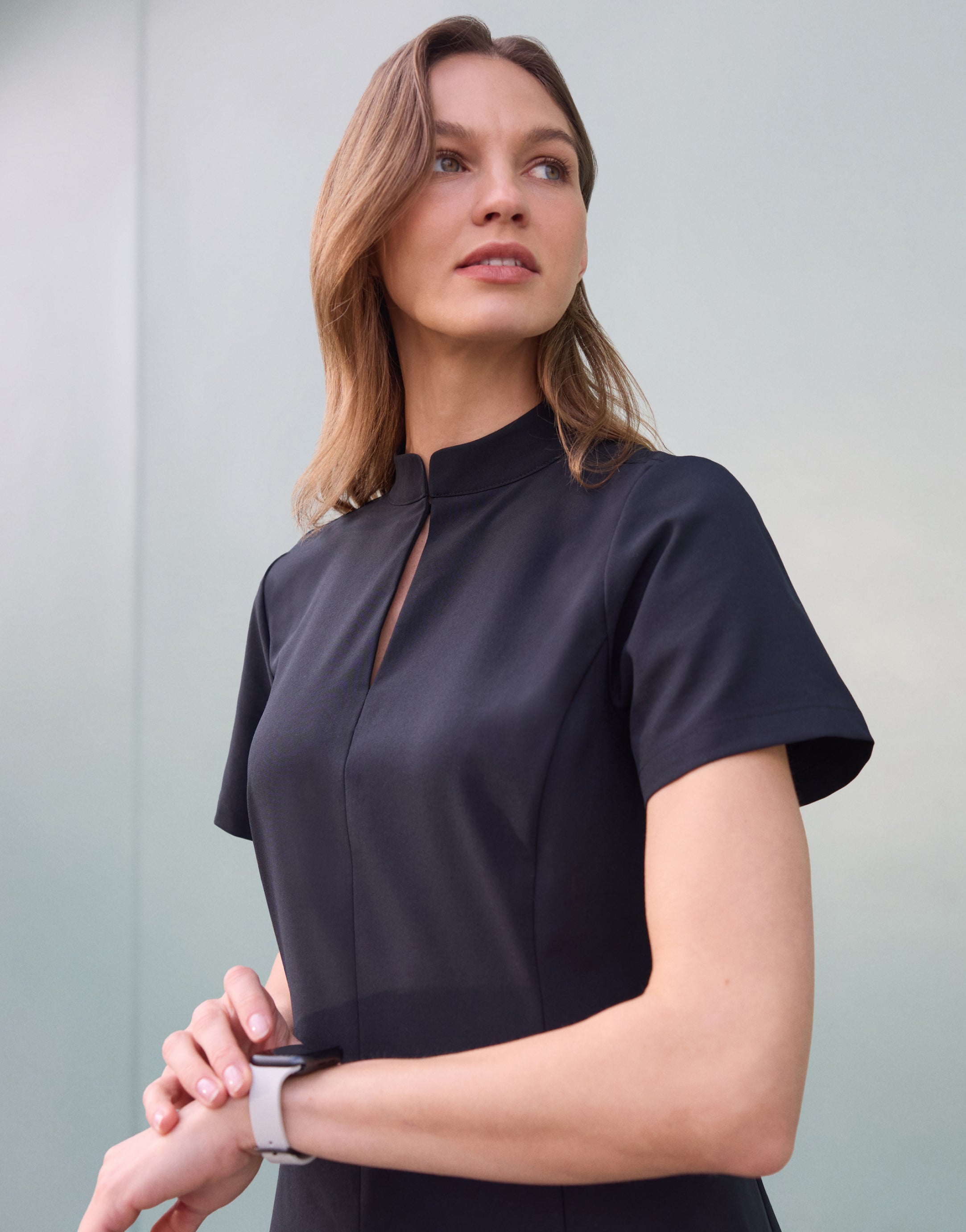 Woman in a black short-sleeve mock-neck scrub top with a keyhole opening, checking her smartwatch