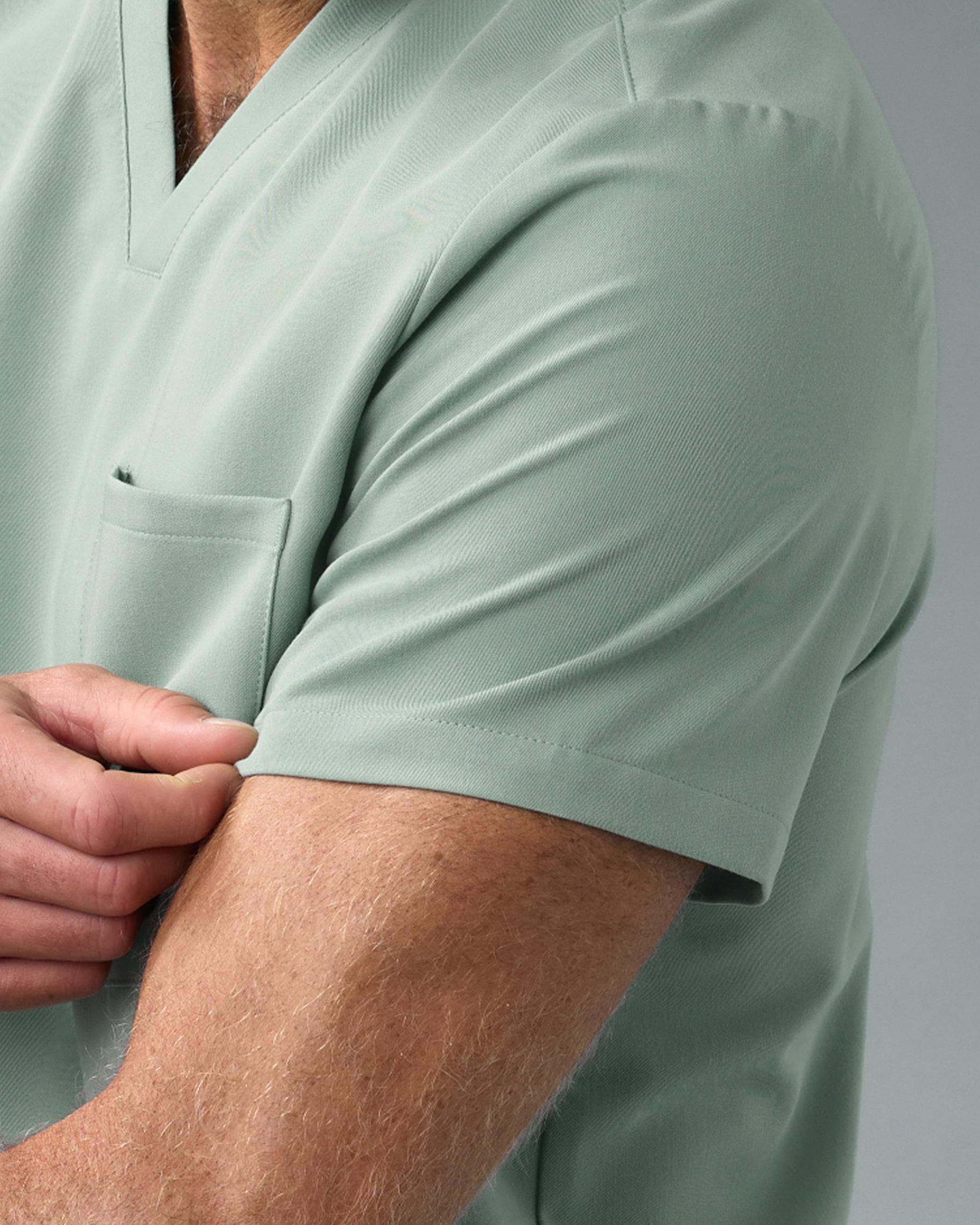 Close-up of the sleeve and chest pocket of a sage green V-neck scrub top